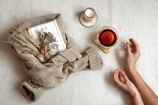 Photo still life with female hands, a cup of tea and dried flowers on a warm sweater, the concept of autumn comfort top view.