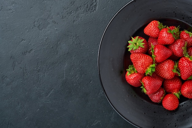 Still life with fresh strawberry in a black bowl. Top view photo of juicy strawberries.Healthy eating concept. Top view with copy space.