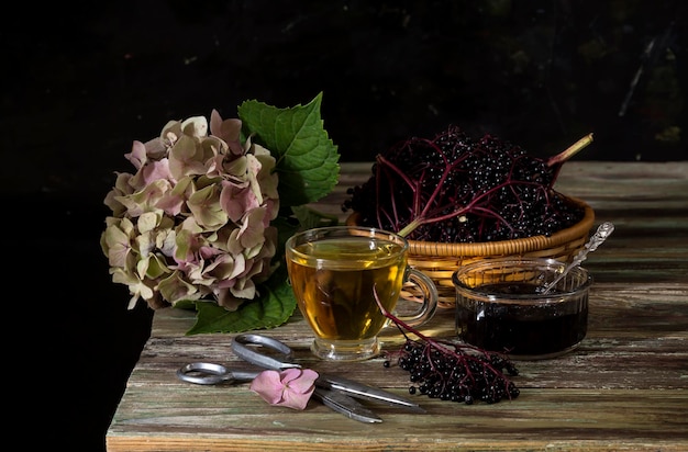 Still life with gentle hydrangea a cup of tea and elderberry jam and a basket of elderberries on a wooden table