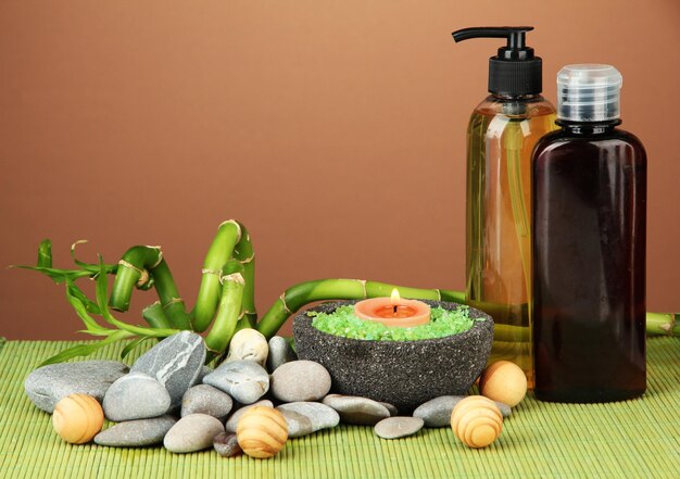 Still life with green bamboo plant and stones on bamboo mat on color background