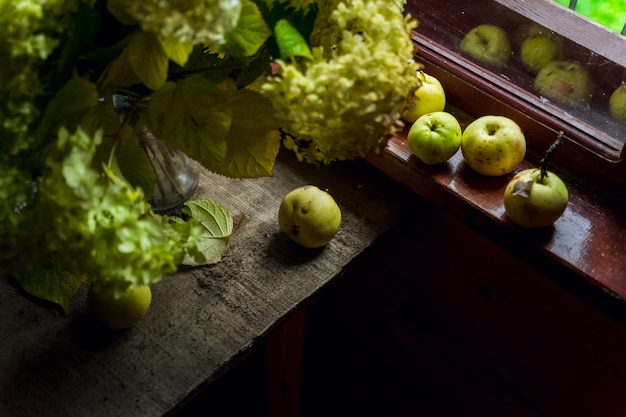 Still life with green hydrangea flowers and a bunch green apples by window of a wooden country house