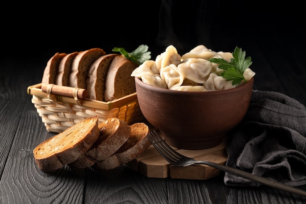 Photo still life with hot dumplings in a clay bowl and toasted rye bread