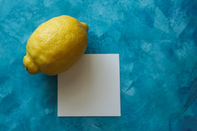 a still life with a lemon and a blank paper card on a bright blue watercolor background