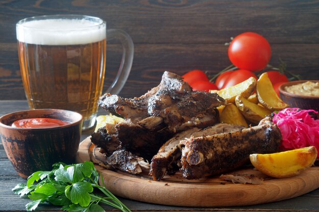 Foto natura morta con boccale di birra e snack - costolette affumicate e spicchi di patate al forno