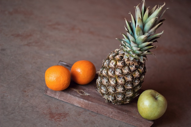 Natura morta con ananas, arance e mela su fondo in legno