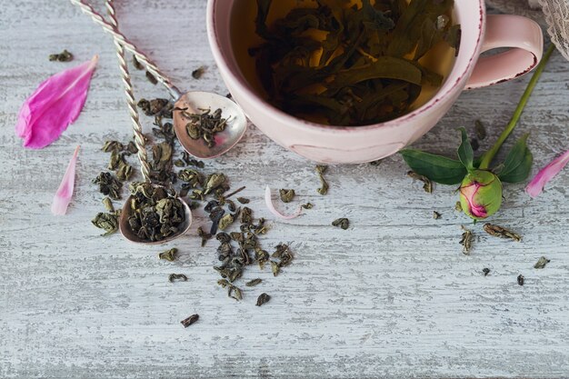 Still life with pink peony flowers and a cup of herbal or green tea on rustic wooden background