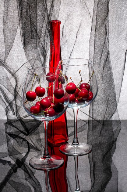 Still life with a red bottle and cherries in glasses