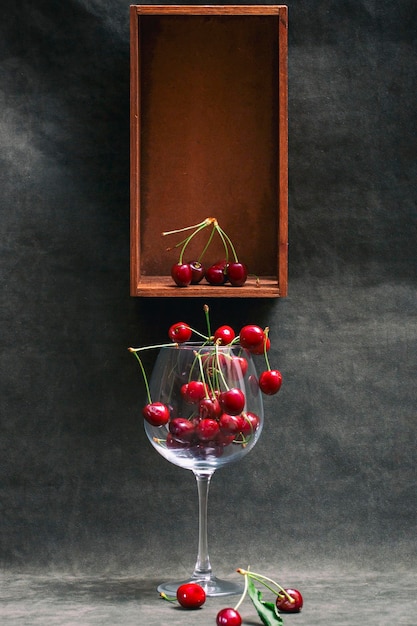 Still life with ripe cherries in a glass and a wooden box