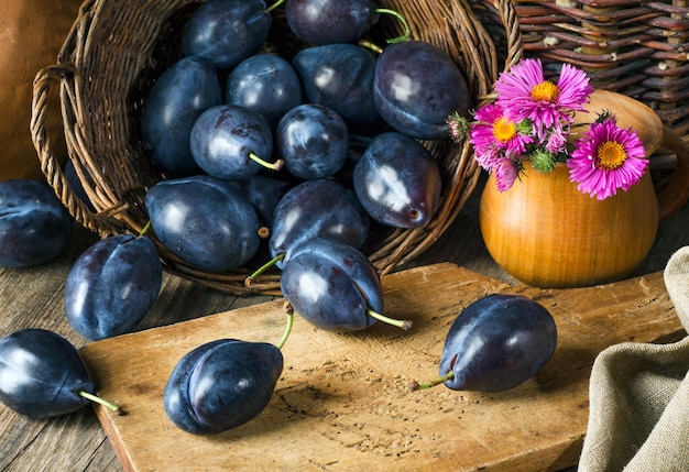 Still life with ripe plums in a basket and pink flowers in rustic style. Ð¡lose-up.