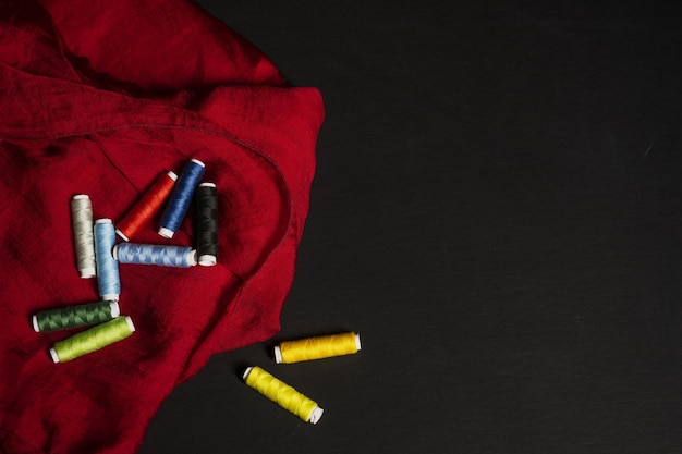 Still life with spools of multicolored thread on a folded subtle red cloth cloth on a black surface