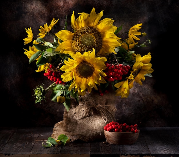 Still life with sunflowers and autumn flowers in a vase on a wooden background