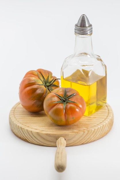 Still life with two tomatoes and an oil can placed on a wooden board on a white background