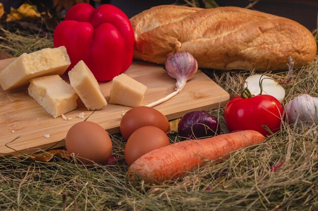 Foto natura morta con verdure e formaggio su un tagliere nel fieno