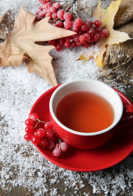 Still life with viburnum  tea in cup, berries and snow, on  wooden background