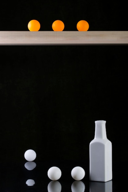 Still life with a white vase and white and yellow balls on a black background