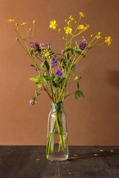 Натюрморт с полевыми цветами в стеклянной бутылке на коричневом фоне современная модная композиция с сушеными ...