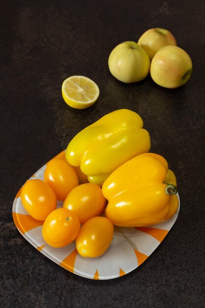 Still life with yellow fruit and vegetables bell pepper tomatoes apples and lemon on a dark background