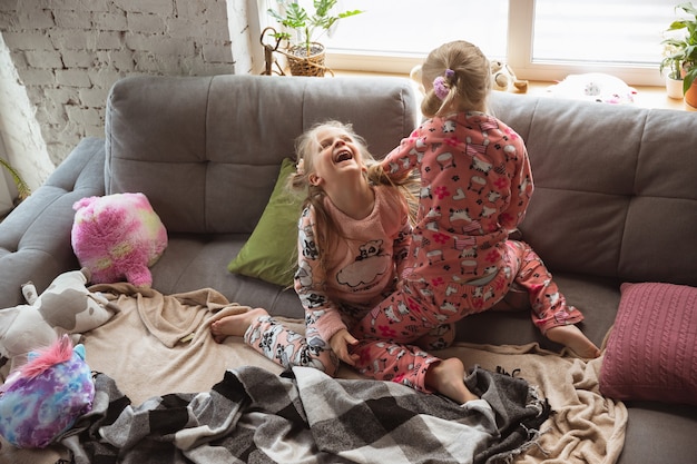 Stille kleine meisjes spelen in een slaapkamer in schattige pyjama's, huiselijke stijl en comfort