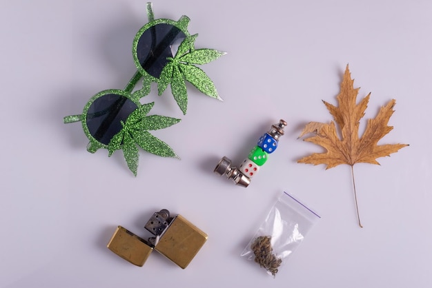 Foto stilleven marihuana zonnebril, aansteker, pak hennep en rookpijp op witte tafel