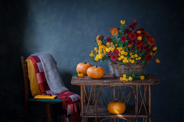 Foto stilleven met chrysanten in mand en pompoenen op houten plank