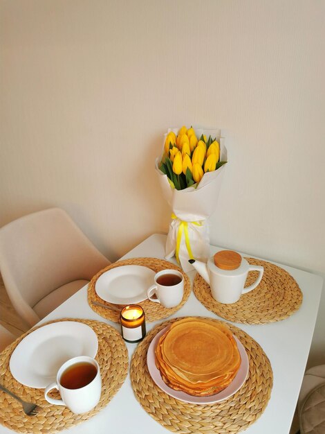 Stilleven met een boeket tulpen een theepot een mok theepannenkoekjes en een kaars