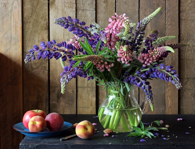 Stilleven met een boeket van lupine in de heldere werper, Apple en perziken