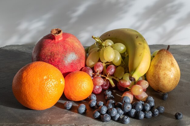 Foto stilleven met een tros druiven, sinaasappels, granaatappel, banaan en bosbessen