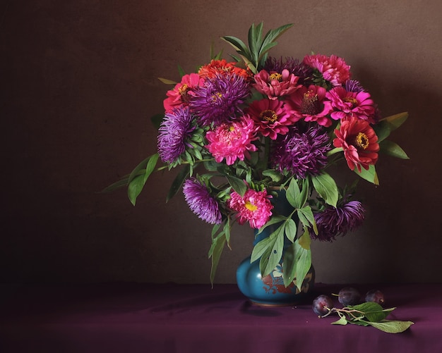 Stilleven met roze en paarse asters en pruimen.