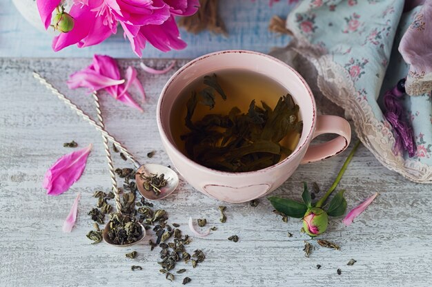 Stilleven met roze pioenbloemen en een kopje kruiden- of groene thee op rustieke houten achtergrond