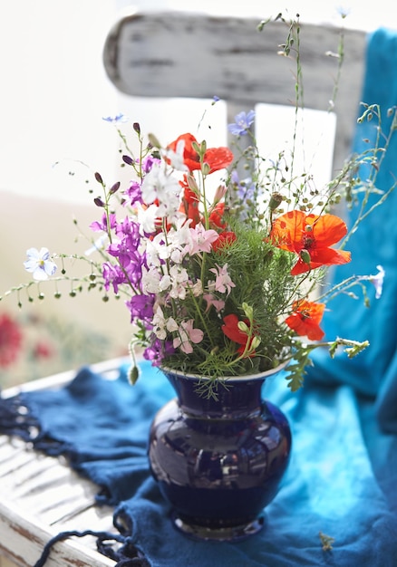 Stilleven met verse wilde bloemen in vaas op vintage stoel