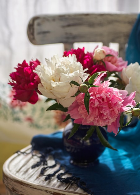 Stilleven met witte en roze pioenrozen in een blauwe vaas op vintage stoel