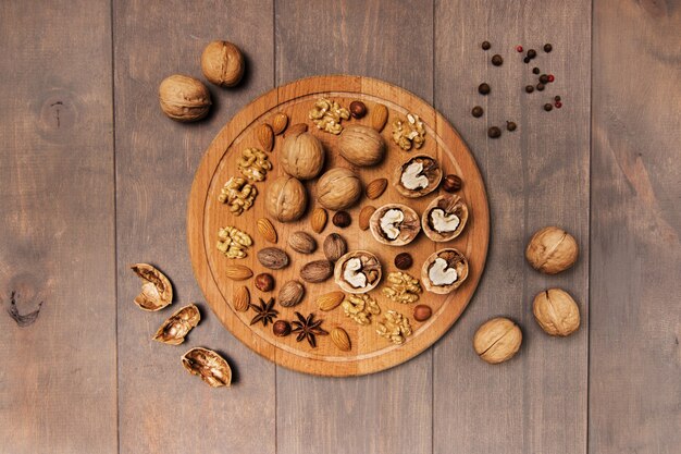 Stilleven. Op een grijze tafel ligt een ronde houten plank. Het bevat hele en gepelde walnoten, amandelen, kruiden. Uitzicht van boven.