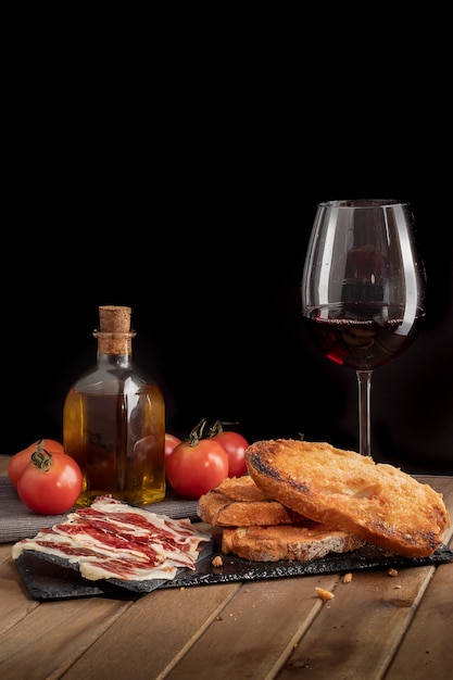 Foto stilleven van iberische ham met tomatenbrood op dienblad van leisteen en glas wijn. zwarte achtergrond.