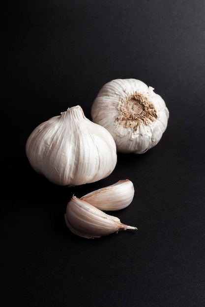 Stilleven van knoflookkoppen en knoflookteentjes op zwarte achtergrond gezonde ingrediënten voedselconcept