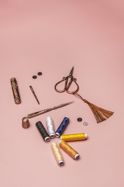 Stilleven van naaigerei met klosjes gekleurde draadjes en vintage koperen schaar op een effen roze achtergrond