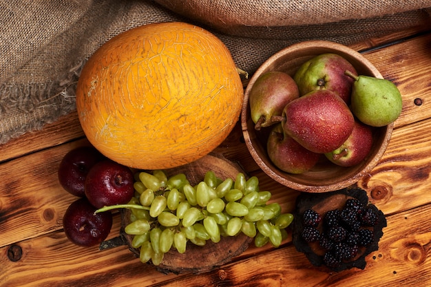 Stilleven van vers fruit met meloen, druiven, pruimen, peren en bramen op een houten tafel