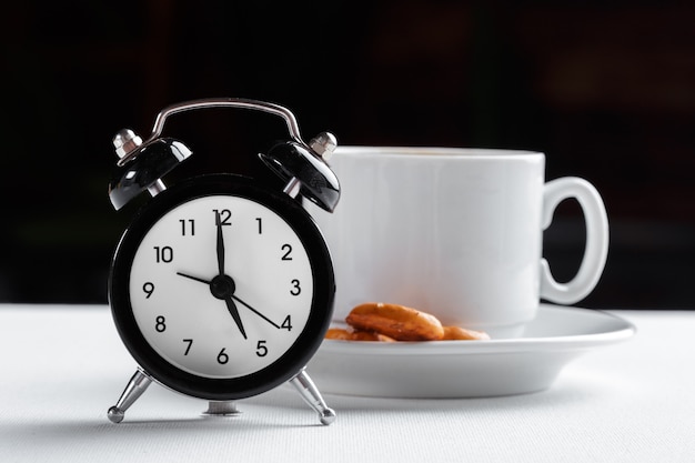 Stilleven, vintage wekker en koffiekopje op witte tafel