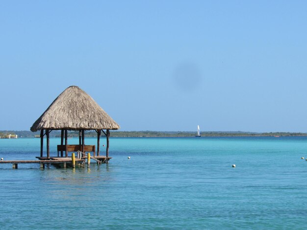 Stilt house on sea against clear blue sky