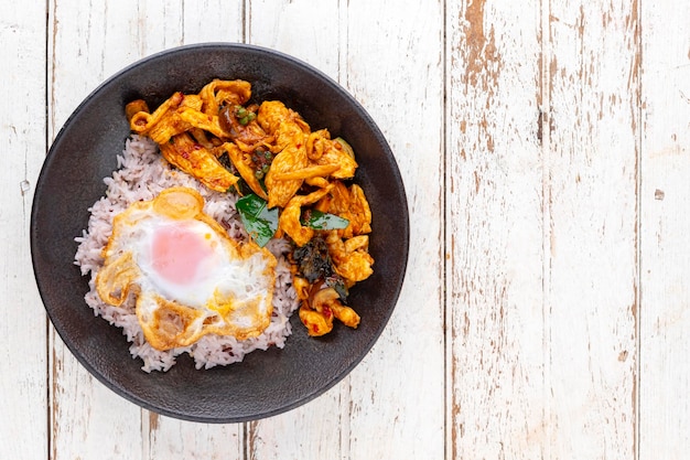 Foto pollo fritto in padella con pasta di curry rosso, foglie di bergamotto, pepe con riso e uova in un piatto di ceramica, vista dall'alto, copia spazio per il testo, cibo tailandese gai pad prik gaeng piccante rosso tailandese saltato in padella