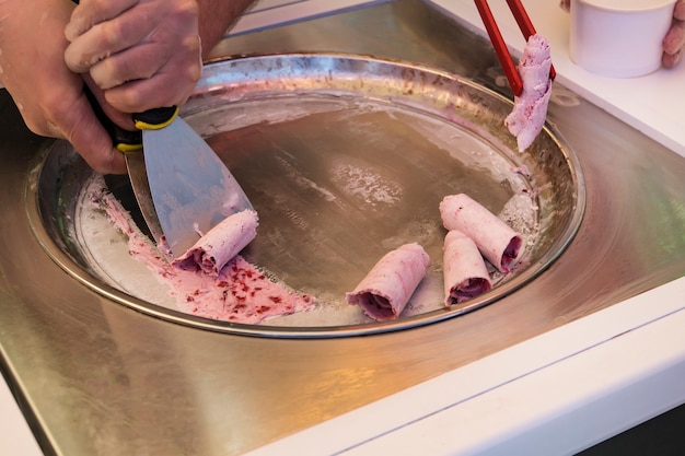 Rotoli di gelato saltati in padella nella padella antigelo. gelato arrotolato, dessert gelato fatto a mano. gelato saltato in padella con latte e marmellata di frutti di bosco. macchina per gelato fritto con vaschetta refrigerata in acciaio