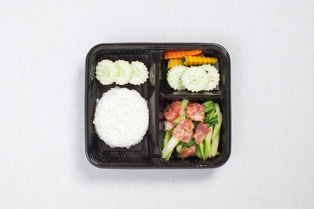Перемешать жареную капусту с беконом и рисом положить в черную пластиковую коробку, положить на белую скатерть, коробку для еды, тайскую еду.