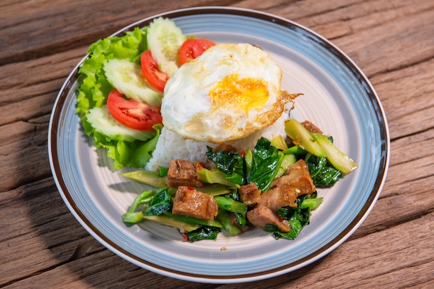 Stir Fried Kale with Crispy Pork with Rice, Serve with lettuce, cucumber, tomato, arrange a beautiful dish, put on a wooden table.