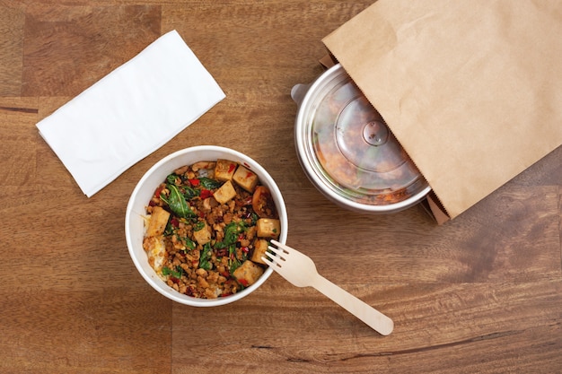 Фото Перемешать жареную свинину и базилик с рисом в бумажной коробке на деревянном фоне