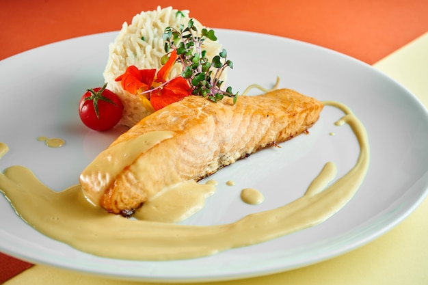 Stir-fried salmon steak with yellow sauce and rice on a side dish in a white plate on colored surface.