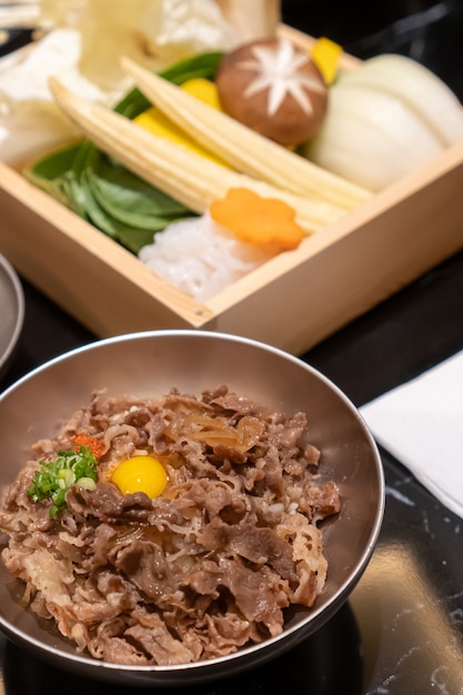 Stir-fried sliced pork with sweet sauce topped on japanese rice topping with a quill egg put in a small stainless steel bowl and various fresh food