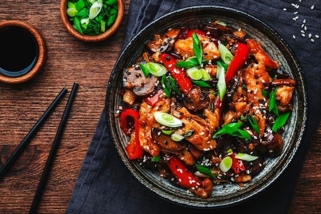 Stir fry chicken with paprika mushrooms and chives in bowl Asian cuisine dish Wooden kitchen table background top view