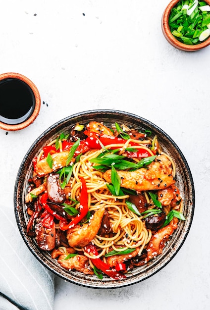 Stir fry egg noodles with chicken sweet paprika mushrooms\
chives and sesame seeds in bowl asian cuisine dish white table\
background top view