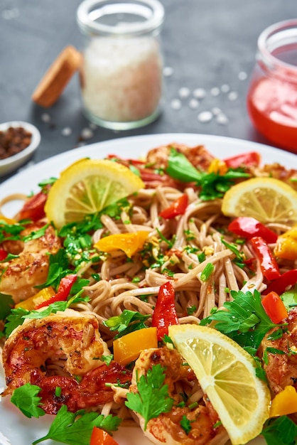 Stir fry noodle with shrimps lemon and fresh parsley on white plate