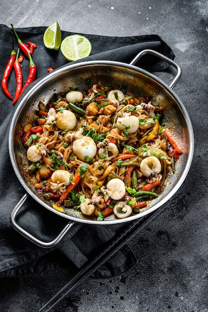 Stir fry noodles with seafood and vegetables in a wok pan. Black surface. Top view