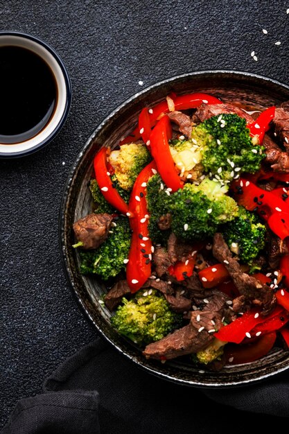 Stir fry vegetables with beef paprika and broccoli with sesame seeds in bowl on black table background top view